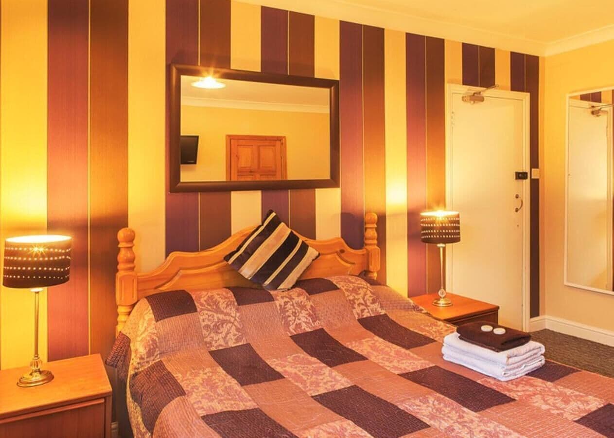 A hotel room with a bed, two bedside lamps, a mirror, and a door.