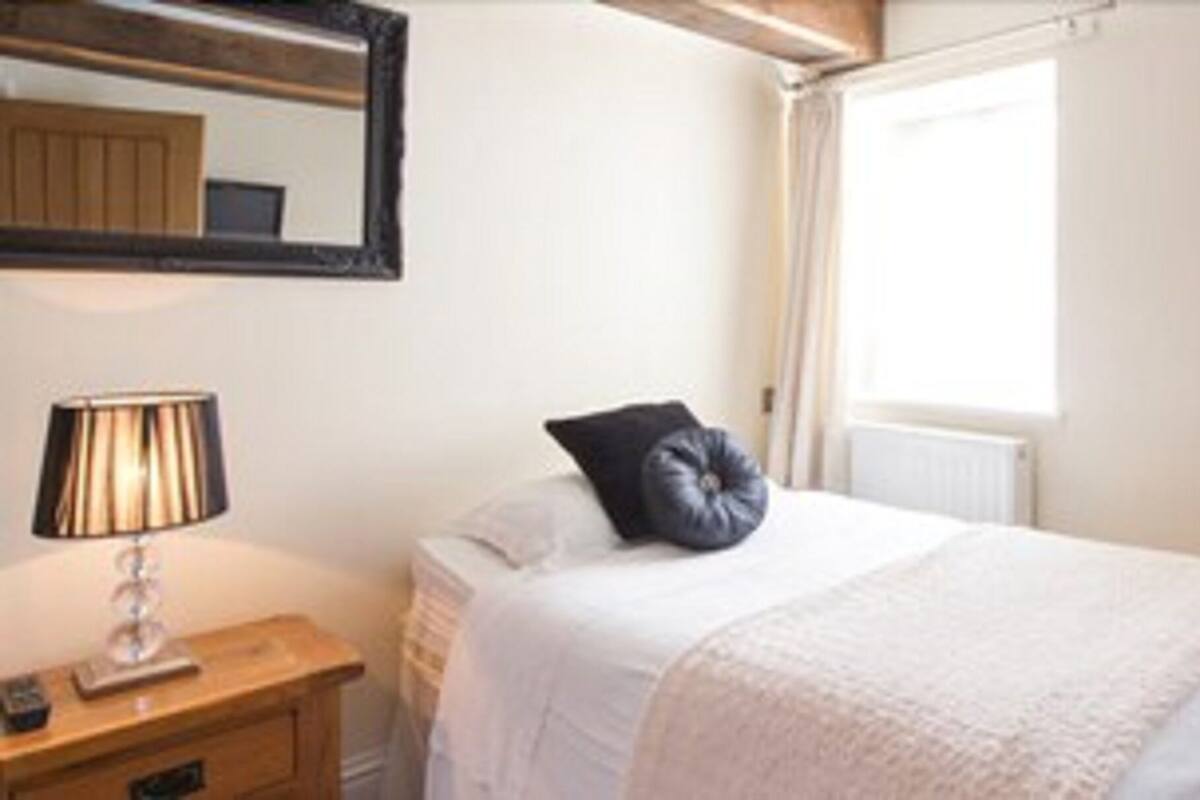A bedroom with a bed, a bedside table with a lamp, a chair, and a desk.