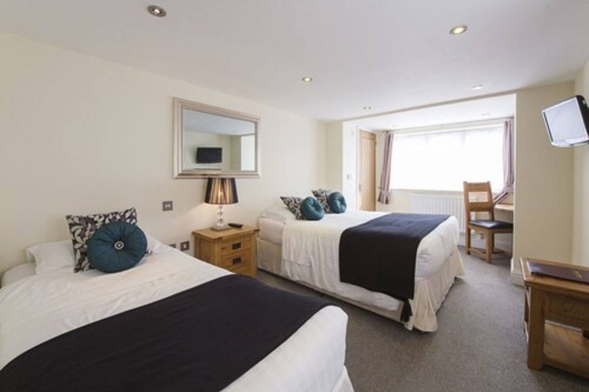 A hotel room with two beds, a desk, a chair, a television, and a window with curtains.