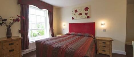 A bedroom with a large bed, a window with curtains, a bedside table, and a wall art piece.