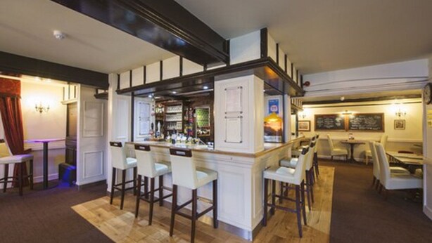 A bar area with a counter, stools, and a seating area with tables and chairs. - The Newtown House Hotel (Hayling Island)