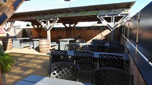 An outdoor patio with wooden tables and chairs, a barbecue grill, and a wooden fence. - Curran Court Hotel (Larne)