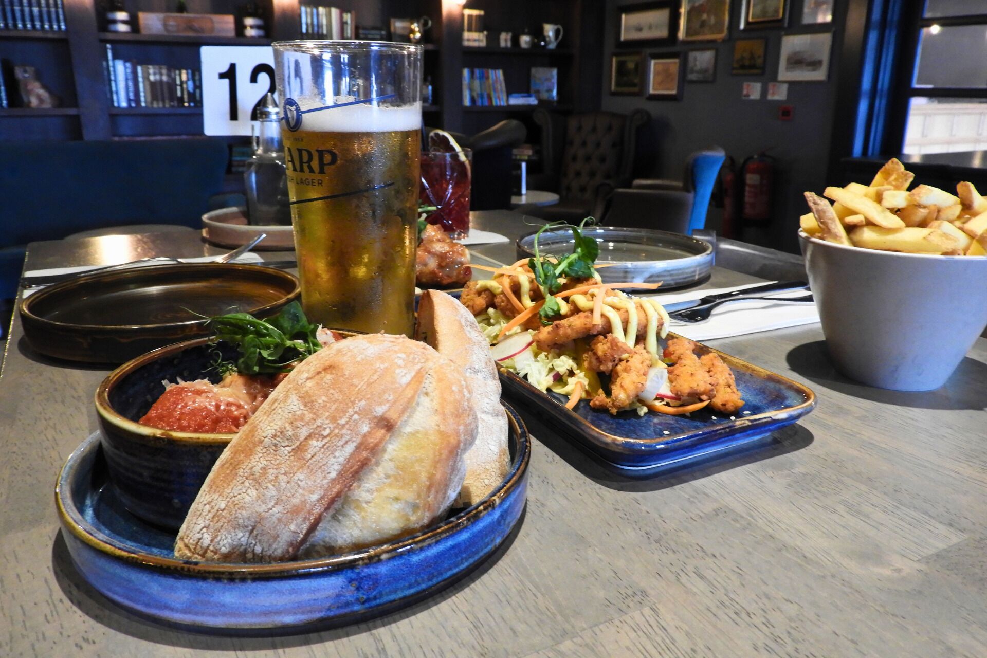 A dining table with a beer glass, bread, salad, and fries.