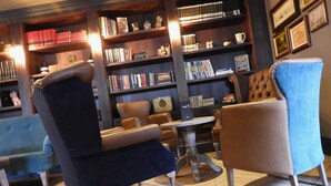 A cozy reading area with leather armchairs, a small round table, and a bookshelf filled with books and decorative items. - Curran Court Hotel (Larne)
