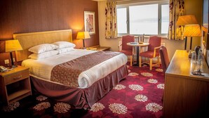 A hotel room with a large bed, a desk with a chair, a small table with two chairs, and a window with curtains. - Curran Court Hotel (Larne)