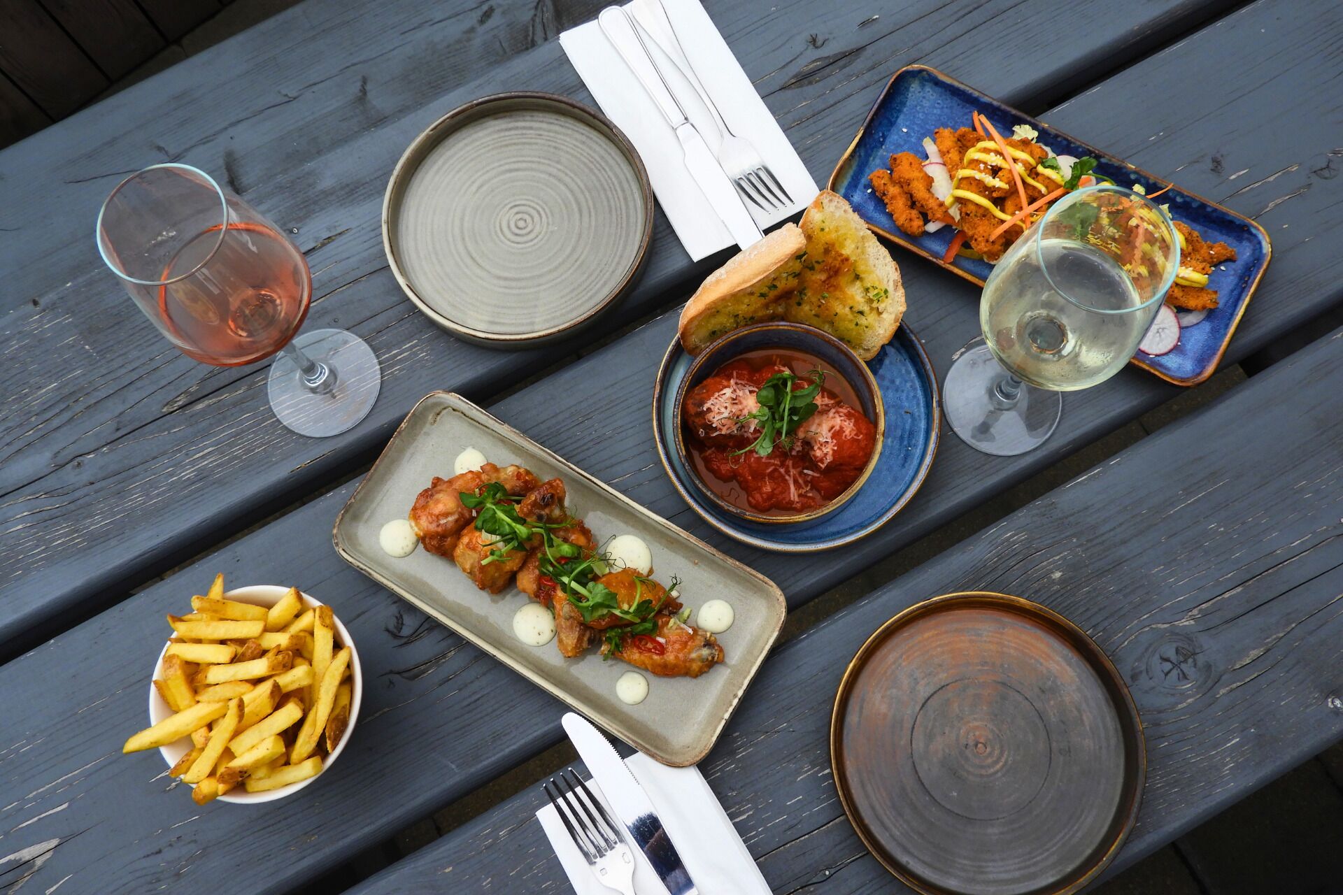 A wooden table with various dishes, including bread, a bowl of fries, and plates of food.
