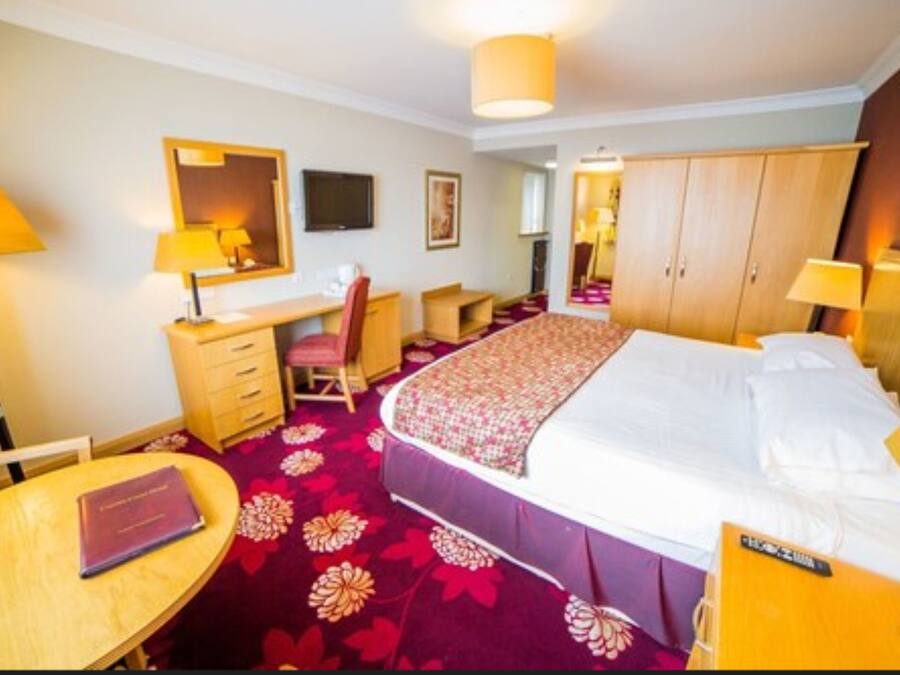 A hotel room with a bed, desk, chair, and a small table.