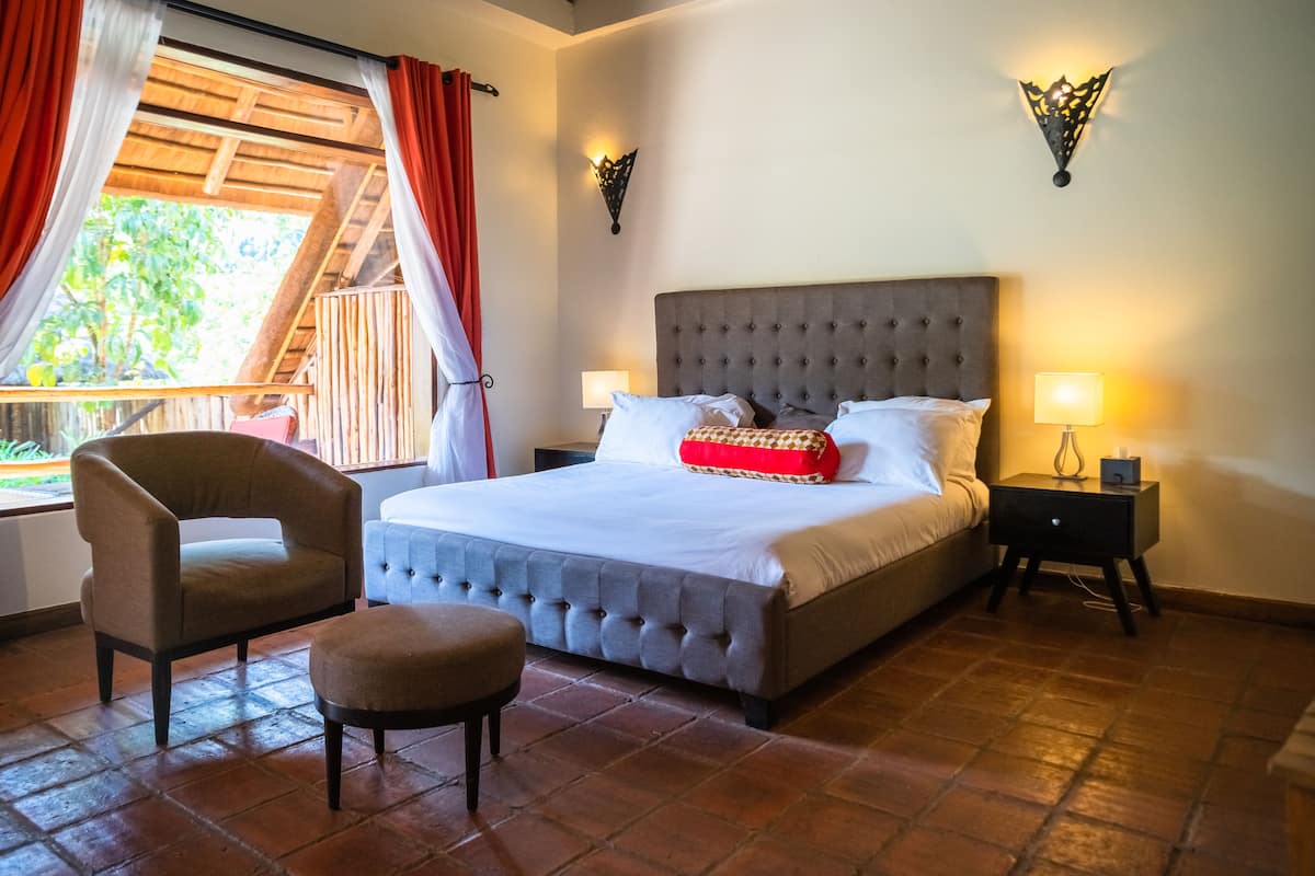 A bedroom with a large bed, two bedside tables, a chair, and a window with curtains.