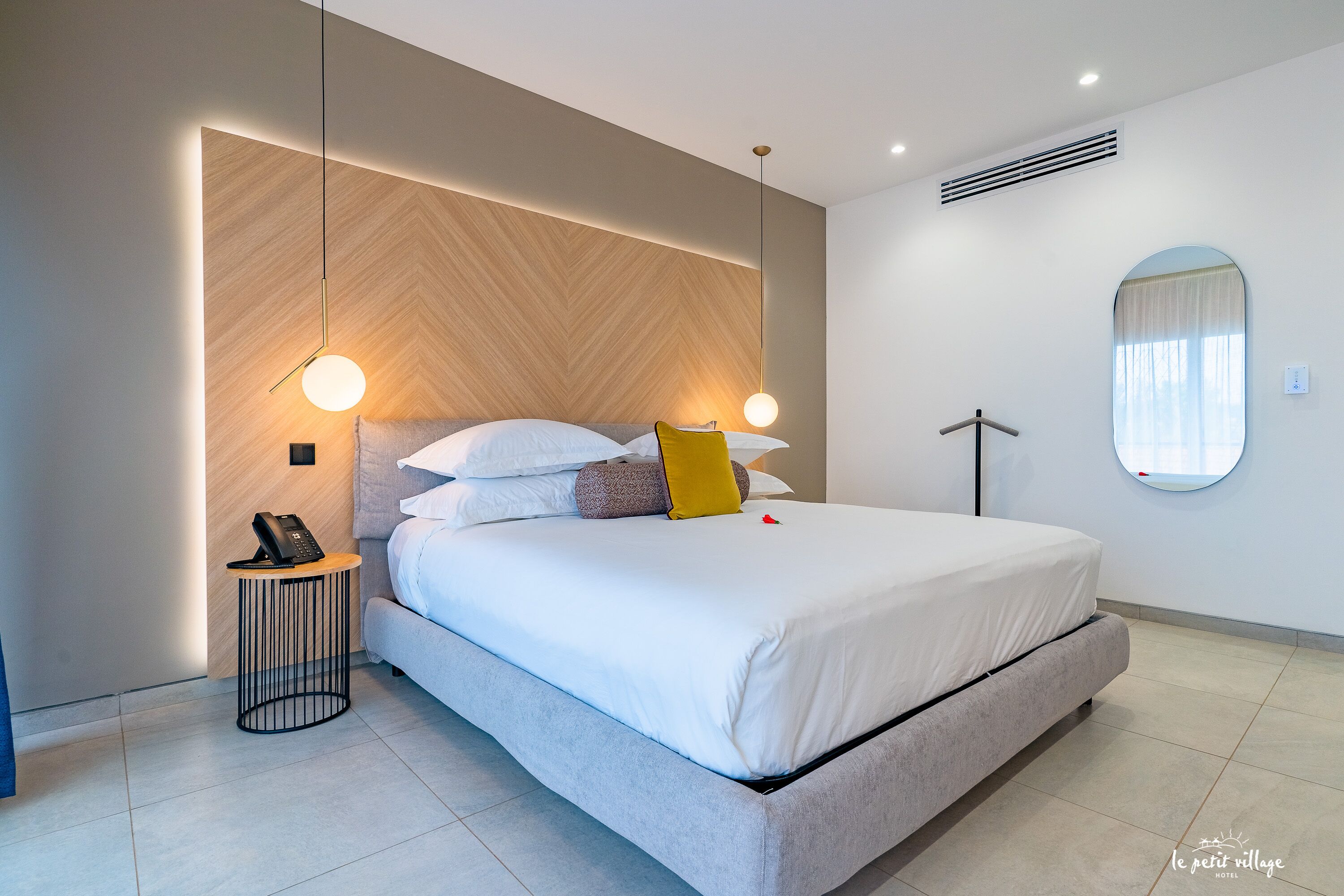 Une chambre d’hôtel moderne avec un grand lit, une table de chevet avec un téléphone et un miroir rond accroché au mur.
