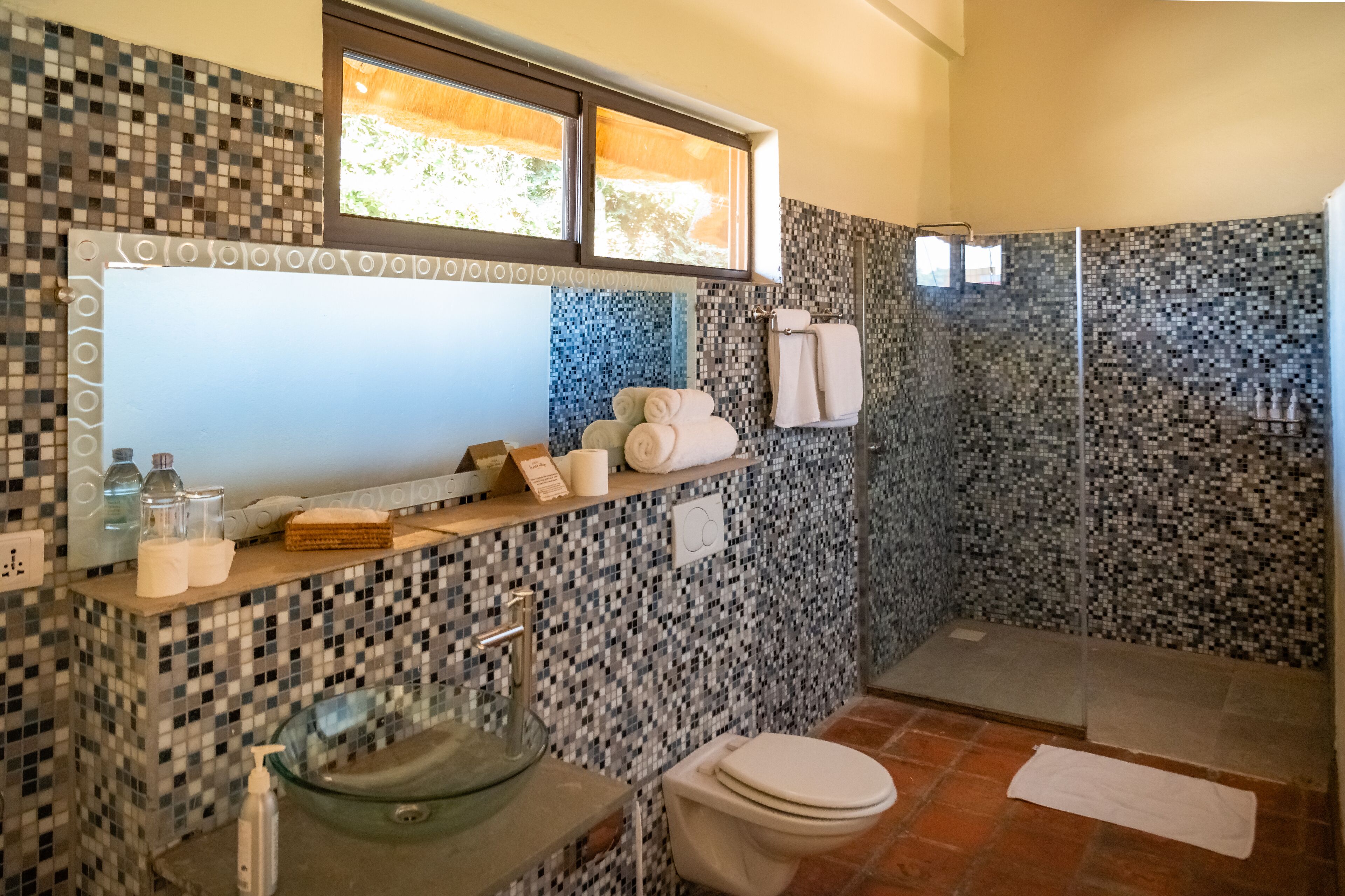 Un baño con pared de mosaicos, un lavamanos de cristal, un inodoro y una zona de ducha.