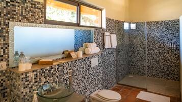 Un baño con pared de mosaicos, un lavamanos de cristal, un inodoro y una zona de ducha.