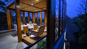 A modern, open-plan dining area with wooden flooring, white furniture, and large windows offering a view of the surrounding landscape. - Le Petit Village Hotel & Spa (Kampala)