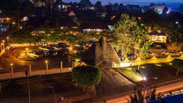 Une vue aérienne nocturne d’une ville, avec une imposante structure en pierre, un rond-point où circulent des voitures et des bâtiments illuminés.