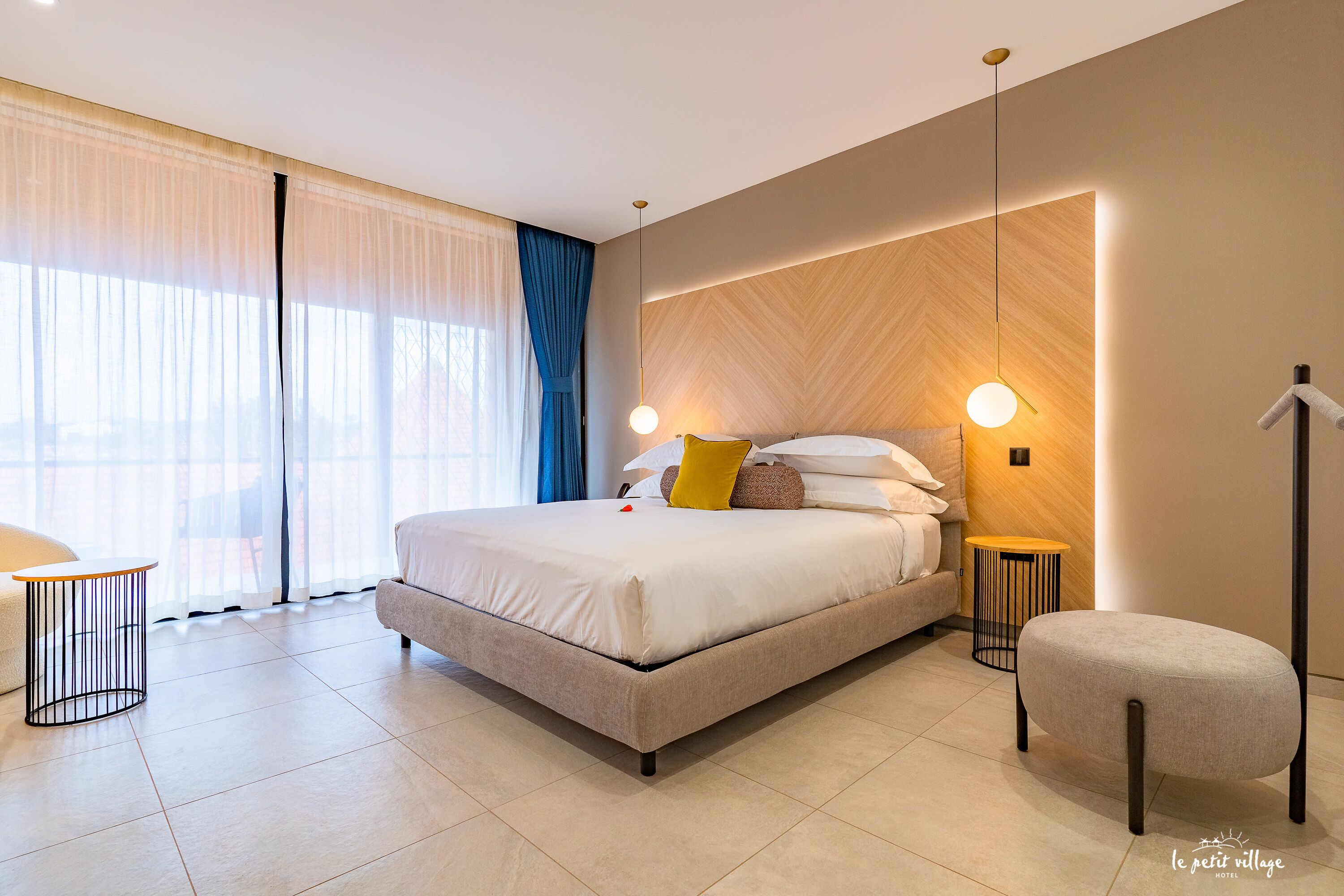 Une chambre d’hôtel moderne avec un grand lit, des tables de chevet, une chaise et une vue sur l’extérieur.
