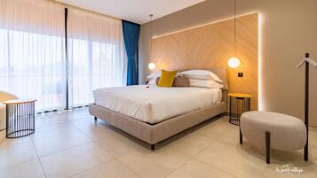 A modern hotel room with a large bed, bedside tables, a chair, and a view of the outdoors.