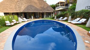 A swimming pool with lounge chairs and a thatched-roof building. - Le Petit Village Hotel & Spa (Kampala)