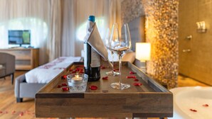 A wooden tray with a bottle, two glasses, a candle, and rose petals on a hotel room table. - Le Petit Village Hotel & Spa (Kampala)