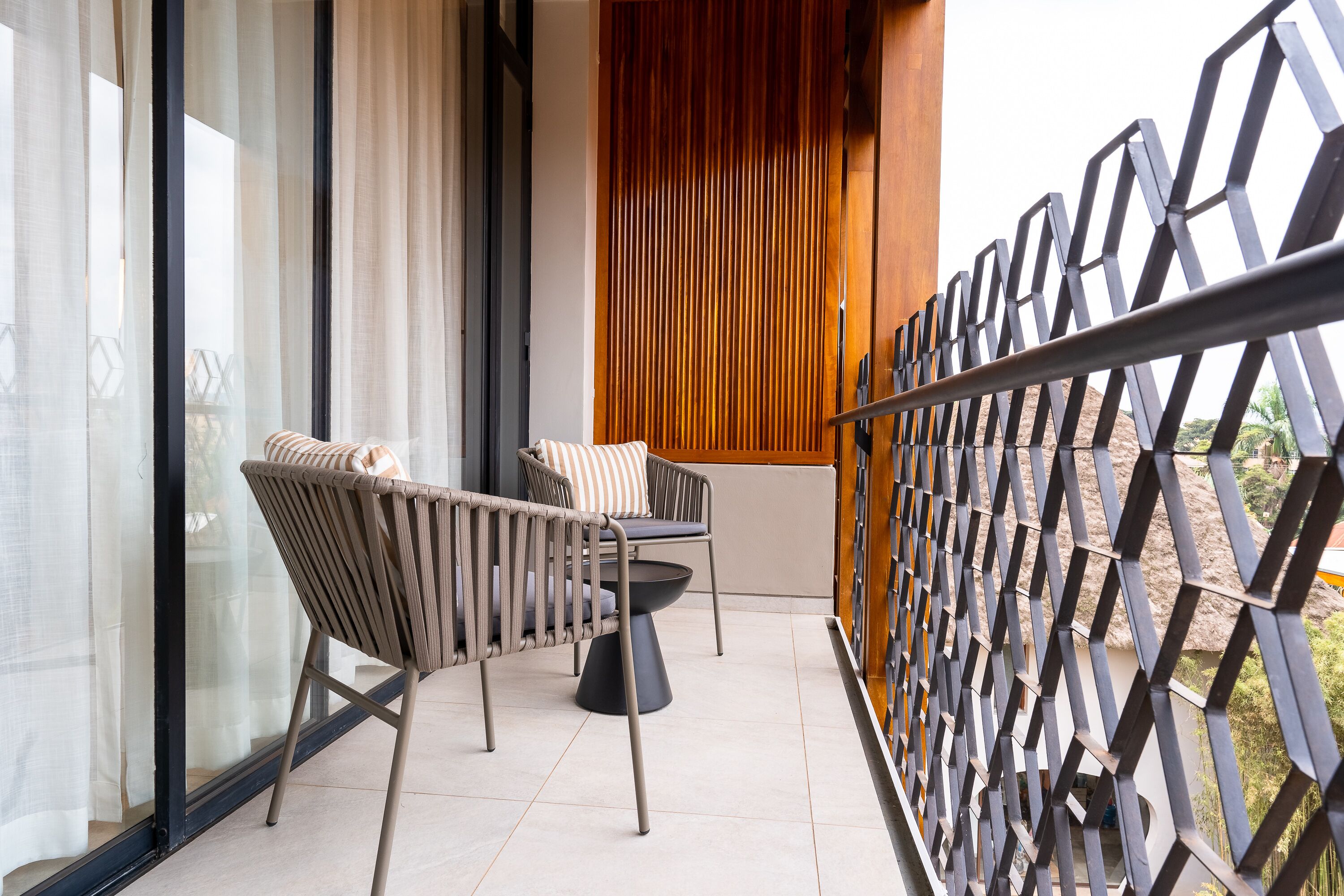 Ein Balkon mit zwei Stühlen, einem Tisch, einer Holz-Schilfwand und einem Metallgeländer.