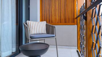 Un balcón moderno con una silla y una mesa, un muro de listones de madera y un cerramiento de vidrio.