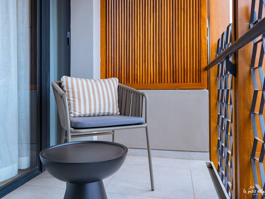 Un balcón moderno con una silla y una mesa, un muro de listones de madera y un cerramiento de vidrio.