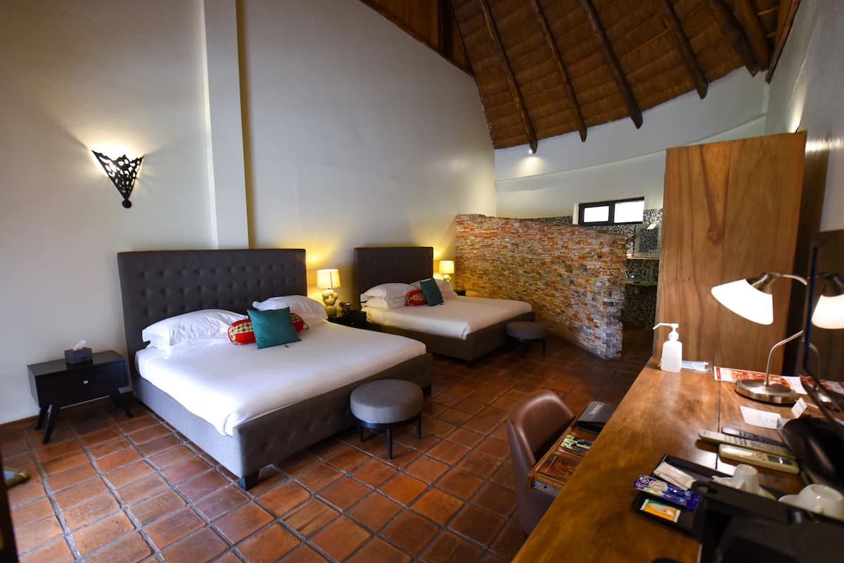 A hotel room with two beds, a wooden desk, a chair, a nightstand, and a bathroom with a shower and a sink.