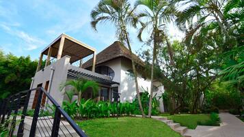 A modern villa with a thatched roof, surrounded by lush greenery and palm trees.