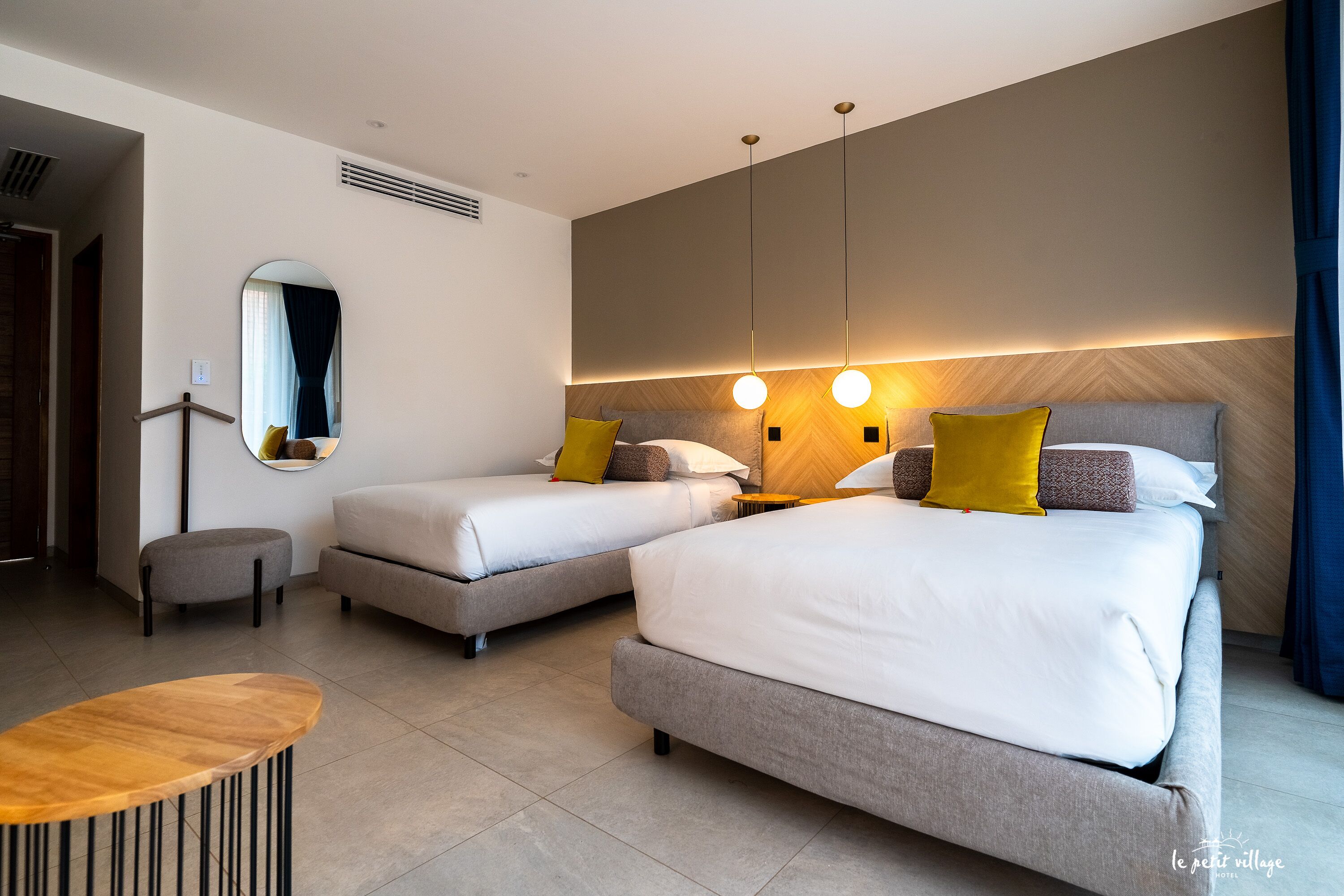 A modern hotel room with two beds, a round table, and a mirror.