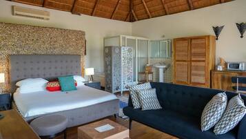 Un dormitorio con cama, mesitas de noche, sofá, escritorio y baño con lavabo y espejo.