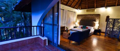 A bedroom with a large bed, a nightstand, a lamp, and a view of palm trees through a glass door.
