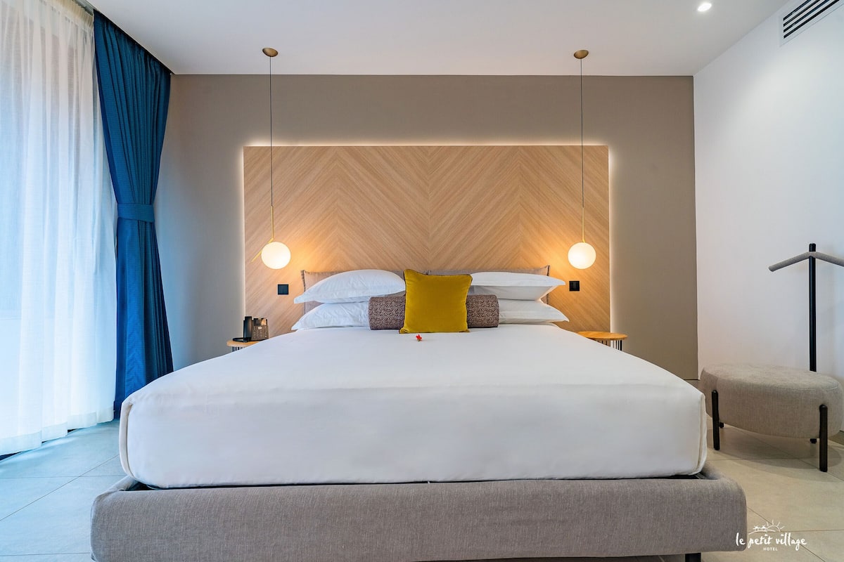 A modern hotel room with a large bed, bedside tables, and a wooden headboard.