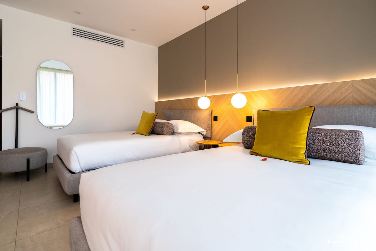 A hotel room with two beds, a round mirror, a small round table, and a wall-mounted light fixture.