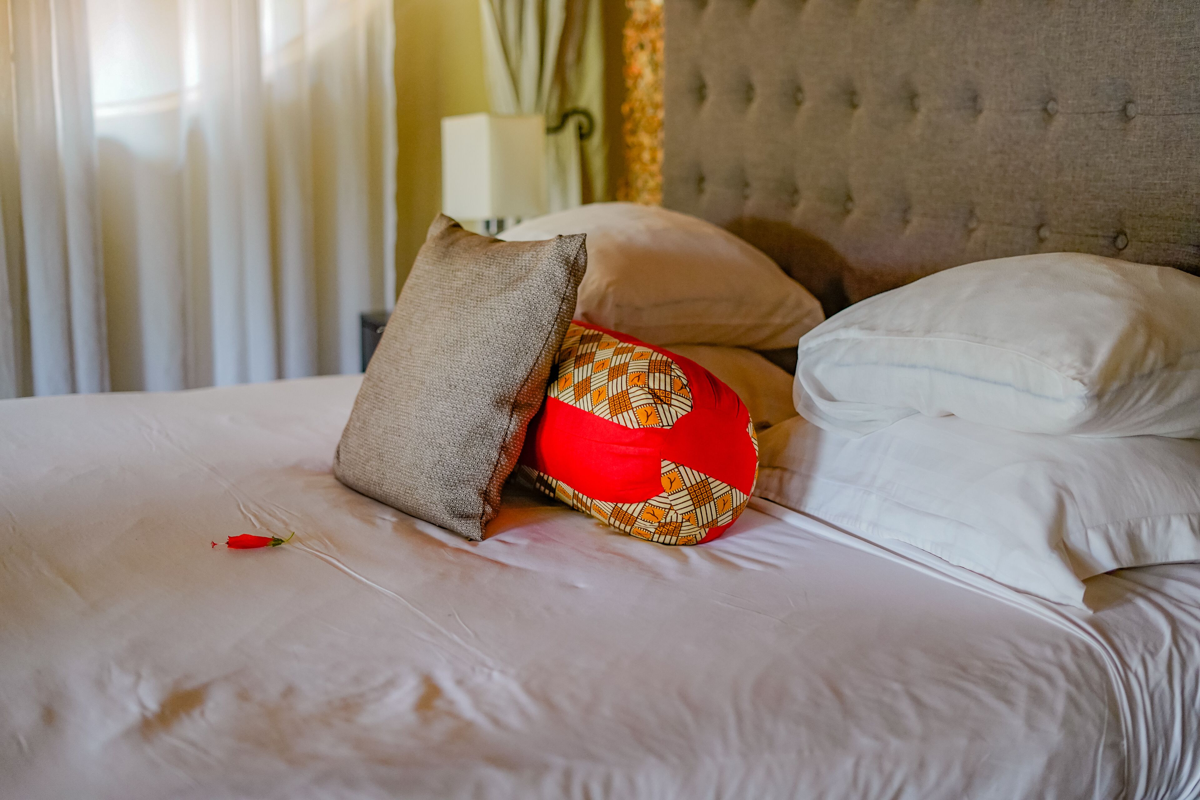 A neatly made bed with a variety of pillows, a tufted headboard, and a lamp in the background.