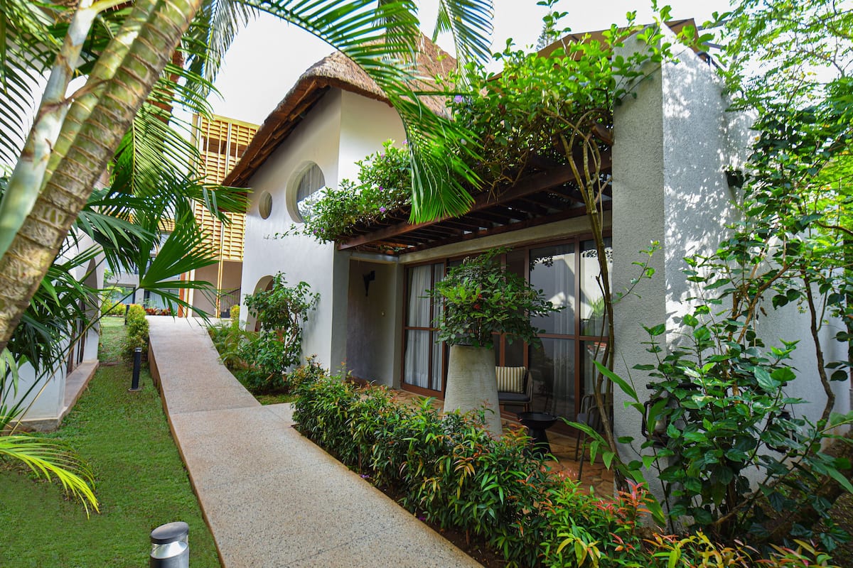 A house with a thatched roof, surrounded by lush greenery and a paved pathway.