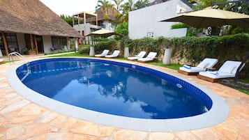 A swimming pool with lounge chairs and umbrellas, surrounded by stone tiles and greenery.