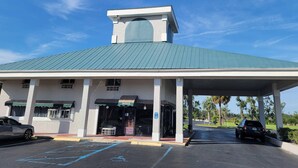 A building with a green roof, a covered entrance, and a parking lot. - Quality Inn Perry (Perry)