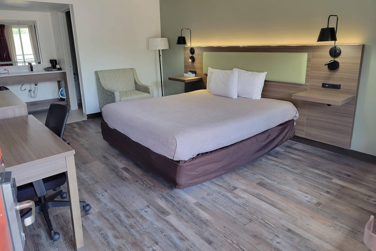 A hotel room with a bed, desk, chair, and a nightstand with lamps.