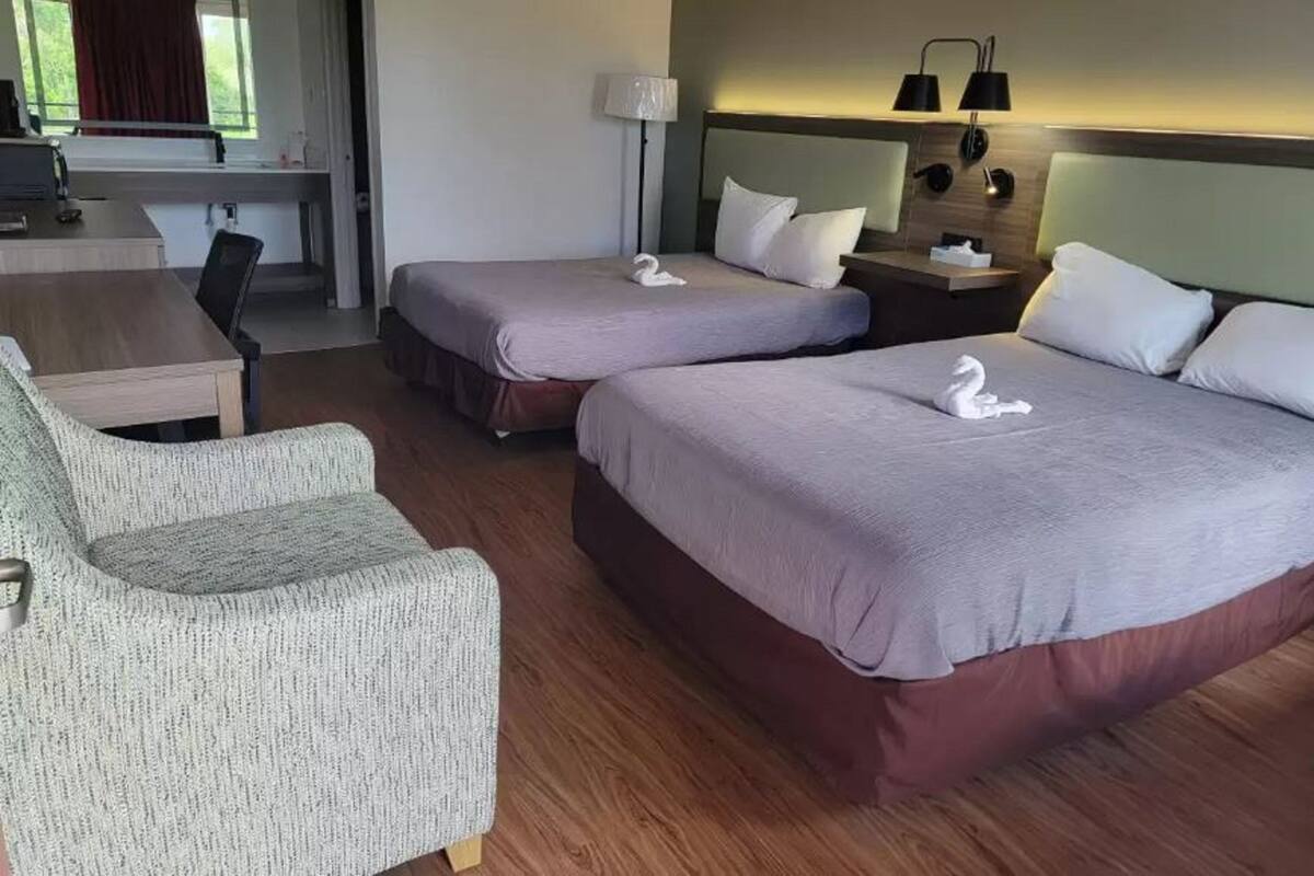 A hotel room with two beds, a desk, a chair, and a lamp.