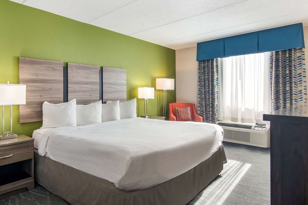 A hotel room with a large bed, two bedside lamps, a chair, a desk, and a window with curtains.