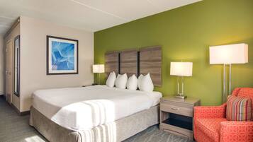 Quarto de hotel com uma cama grande, duas mesas de cabeceira com luminárias, uma cadeira vermelha e uma parede verde decorativa.