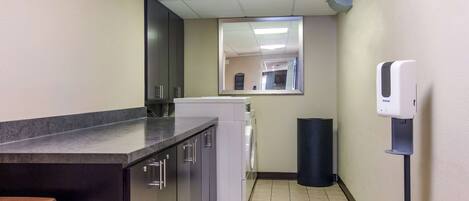 A compact kitchen with a built-in washer and dryer, a trash bin, and a hand sanitizer dispenser.