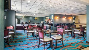 Een hotel lobby met een gekleurd tapijt, houten stoelen, tafels, een bar en een keuken op de achtergrond.