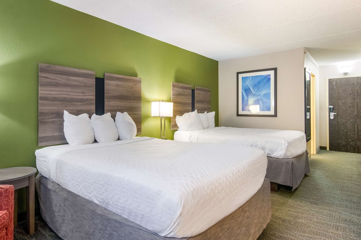 A hotel room with two beds, a green wall, a framed picture, and a lamp.