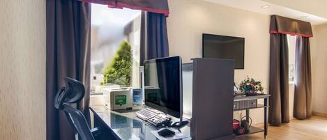 A hotel room with a desk, computer, and a view of a tree outside.