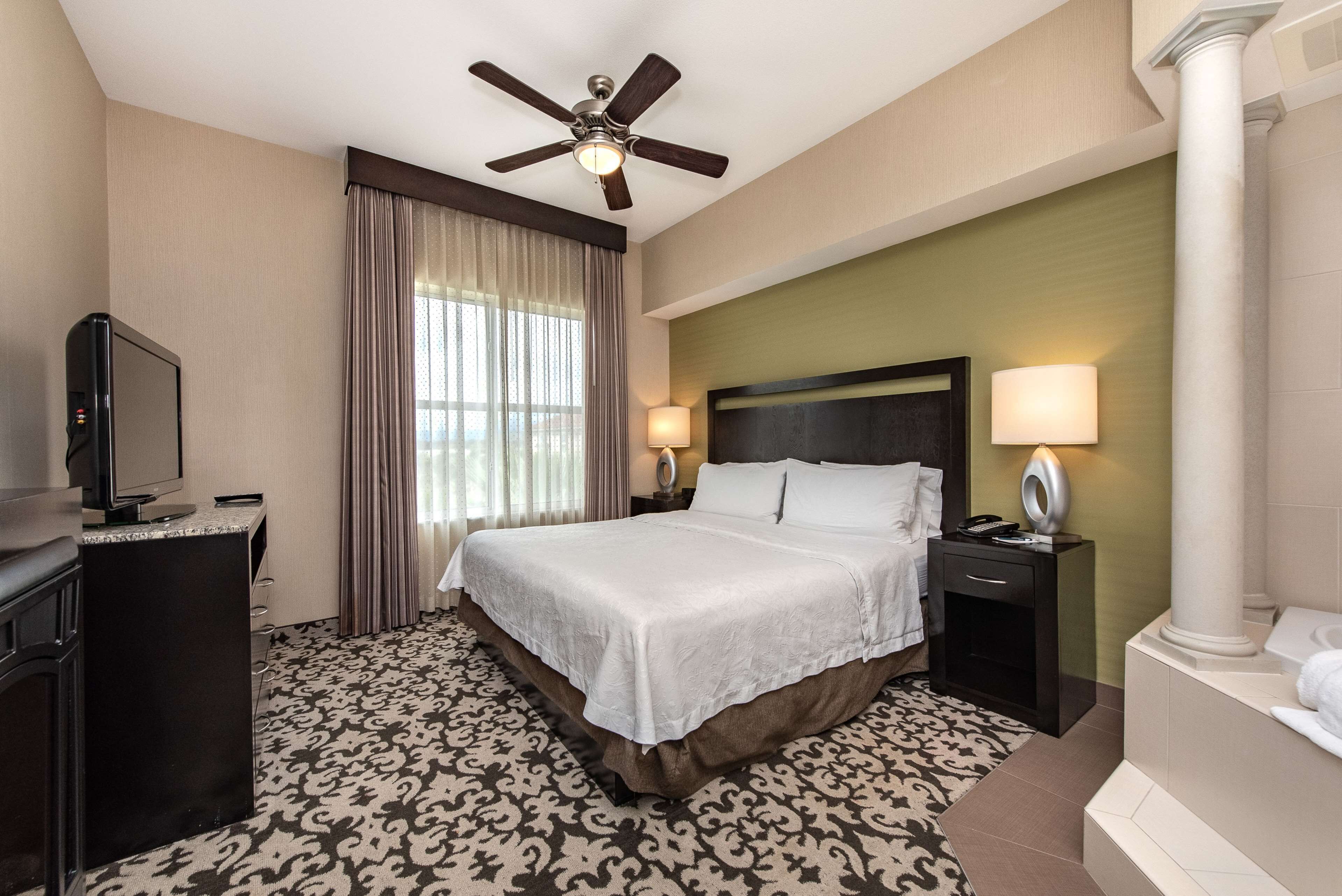 Une chambre d’hôtel comprenant un lit, un bureau avec une télévision, une table de chevet avec une lampe et une salle de bain avec une baignoire.