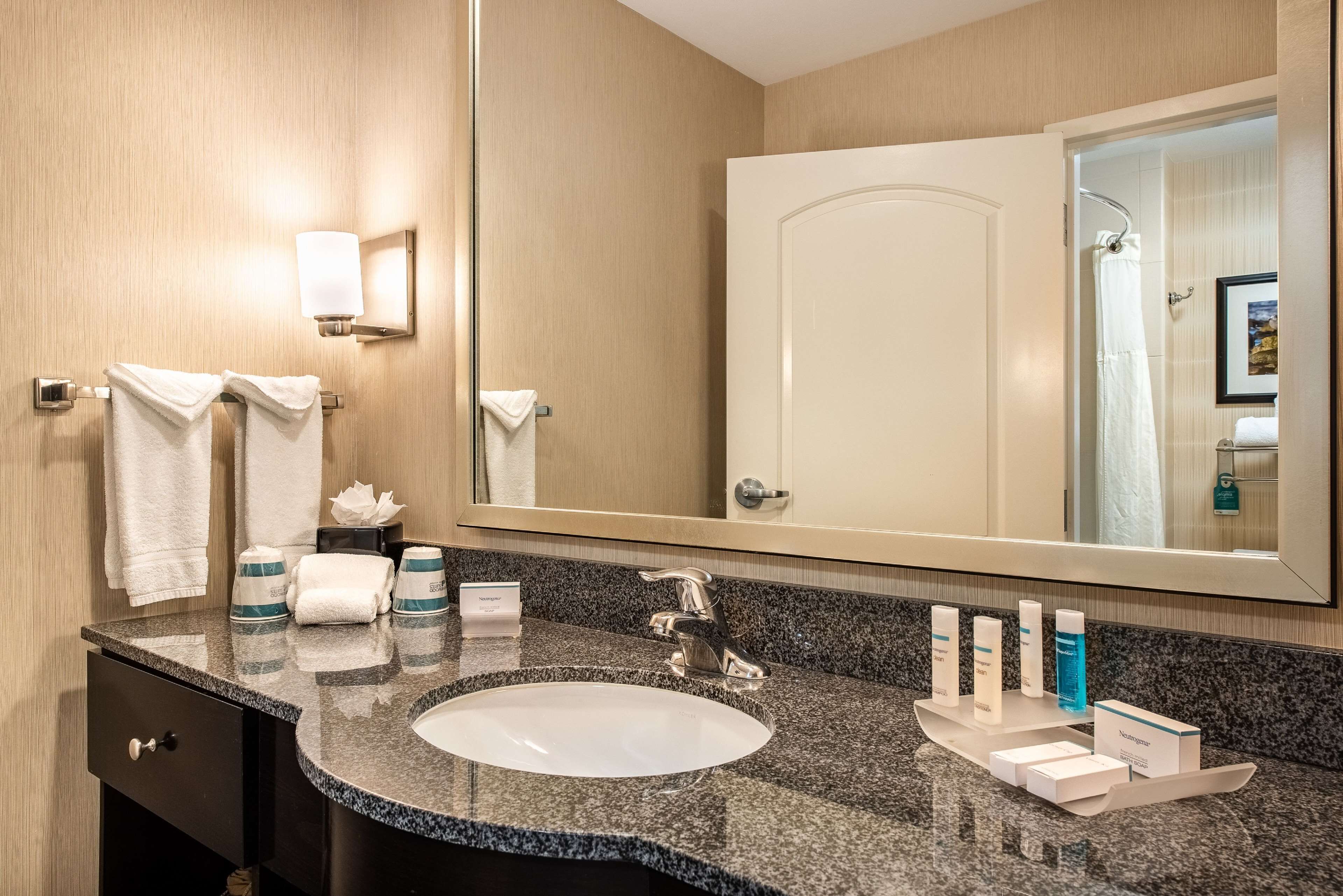 A hotel bathroom with a granite countertop sink, a large mirror, and toiletries on the counter.