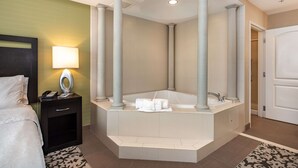 A hotel bathroom with a large bathtub, a bedside table with a lamp, and a bed. - Homewood Suites by Hilton Oxnard/Camarillo (Oxnard)