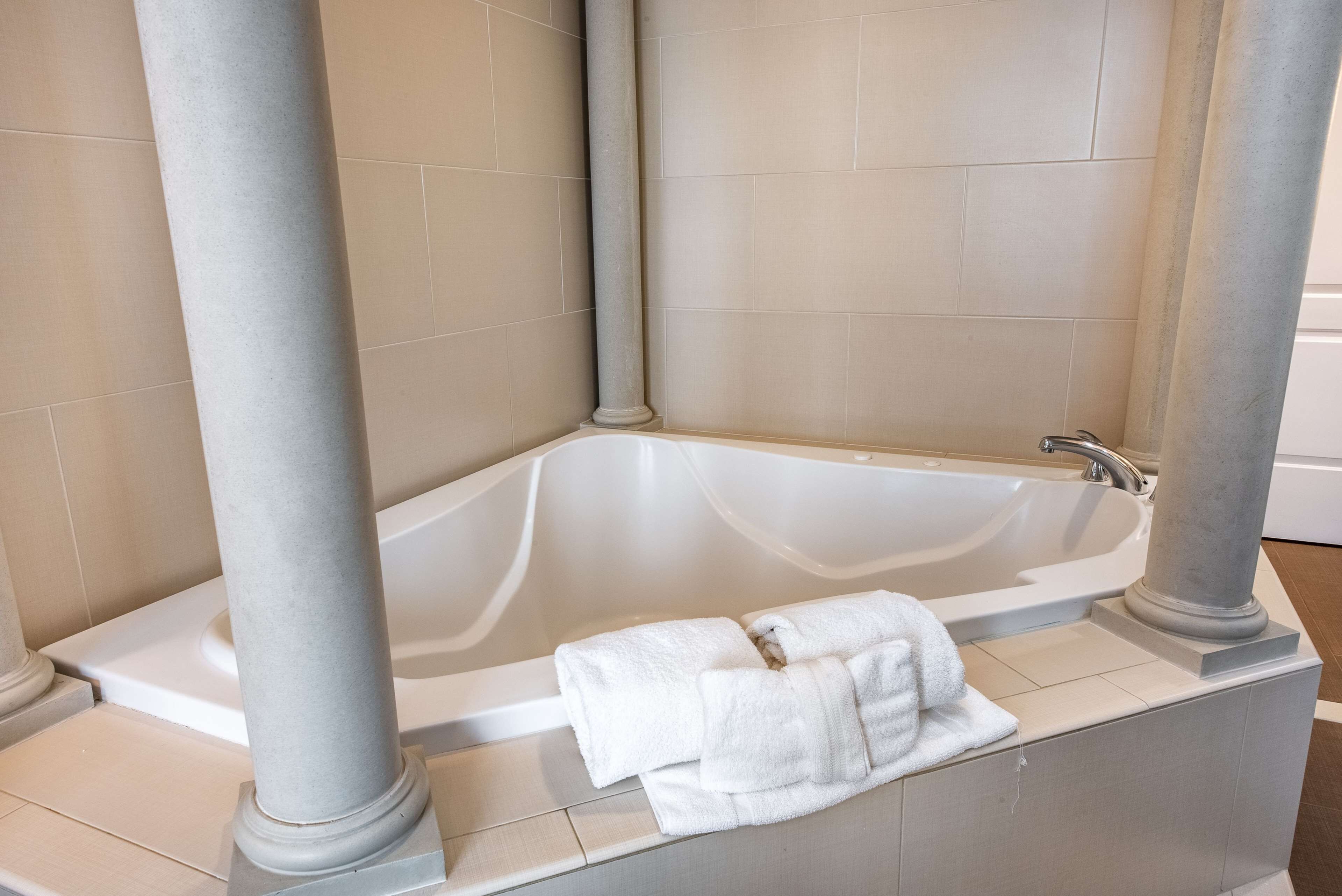 Una bañera de esquina con una toalla, azulejos color crema y columnas.