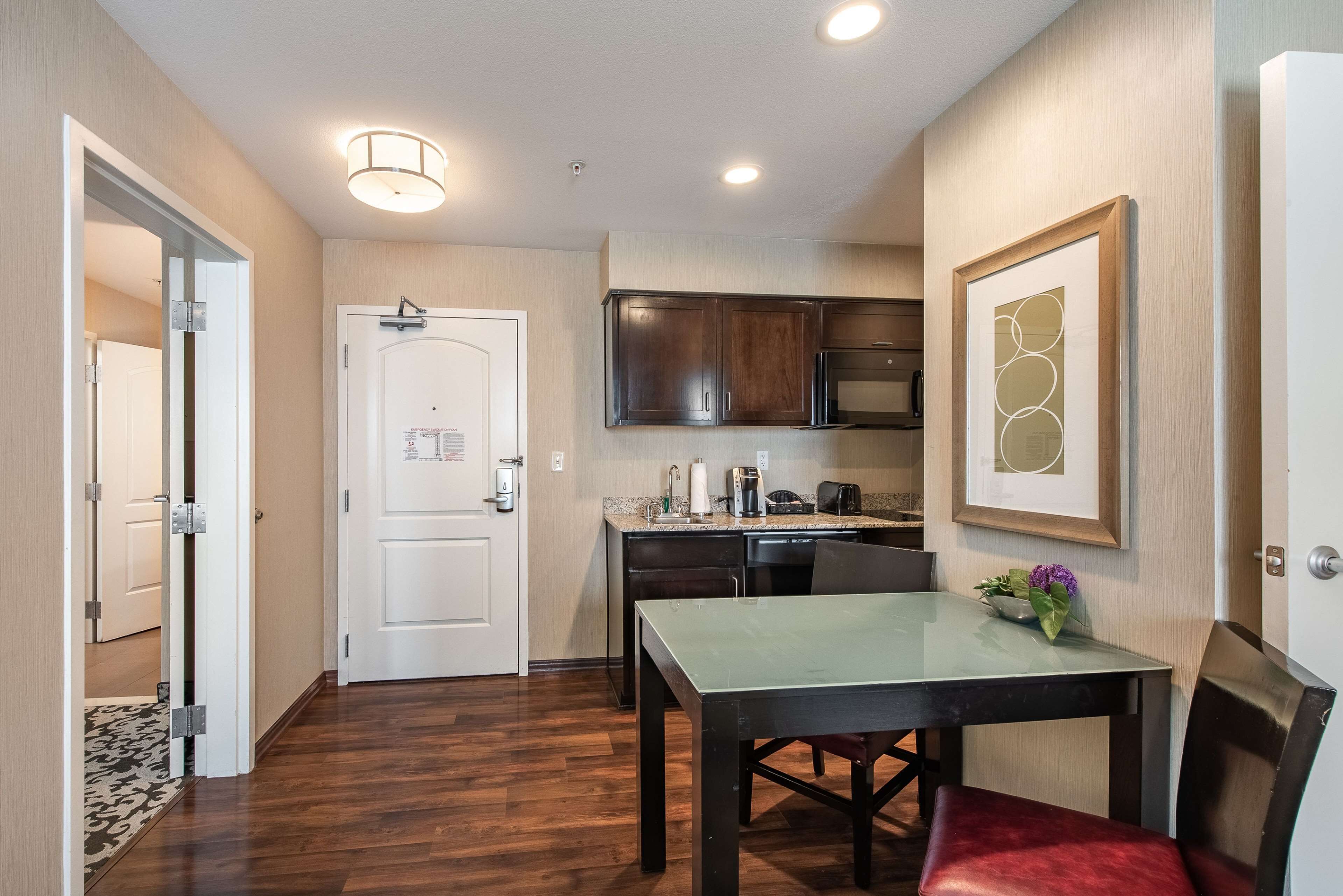 A modern kitchen with dark wood cabinets, a stainless steel microwave, and a small dining area with a table and chairs.