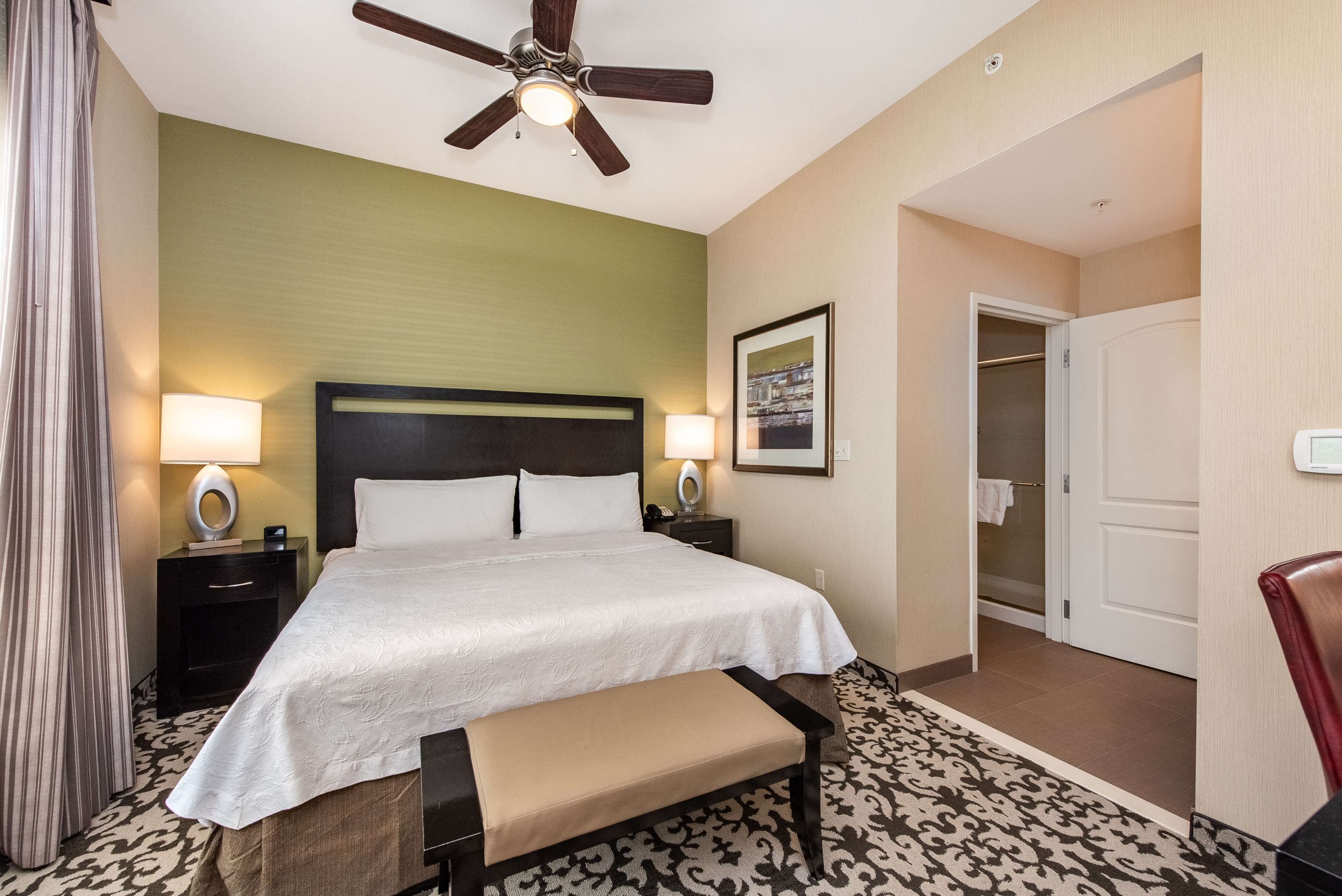 A hotel room with a bed, bedside lamps, a ceiling fan, a patterned rug, and a door leading to a bathroom.