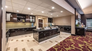 A modern kitchen with dark cabinetry, a central island, and a patterned carpet. - Homewood Suites by Hilton Oxnard/Camarillo (Oxnard)
